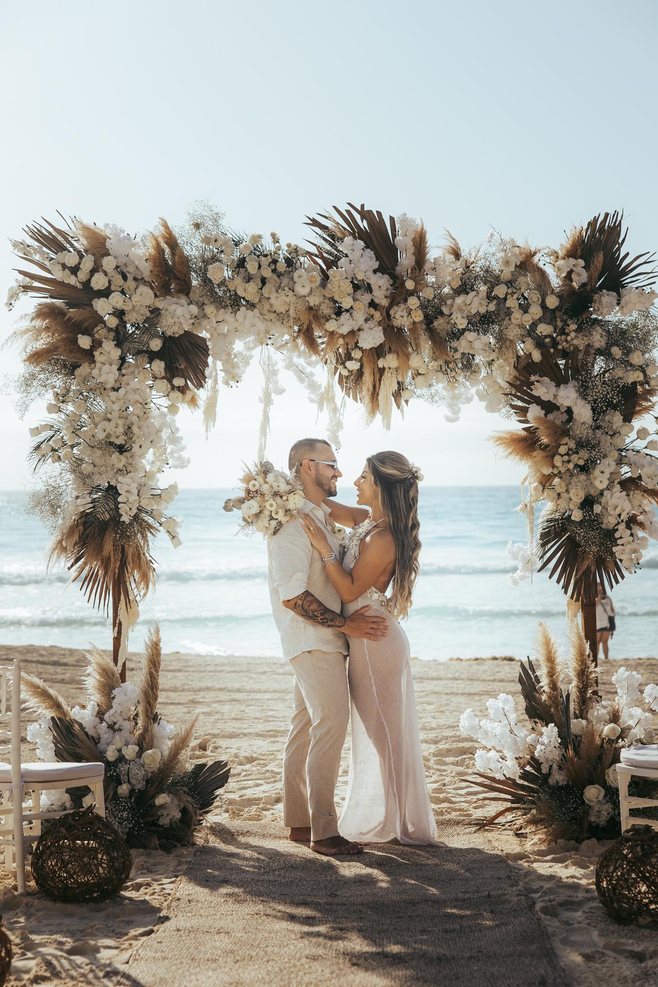Momento romântico sob arco de flores brancas e folhagens douradas